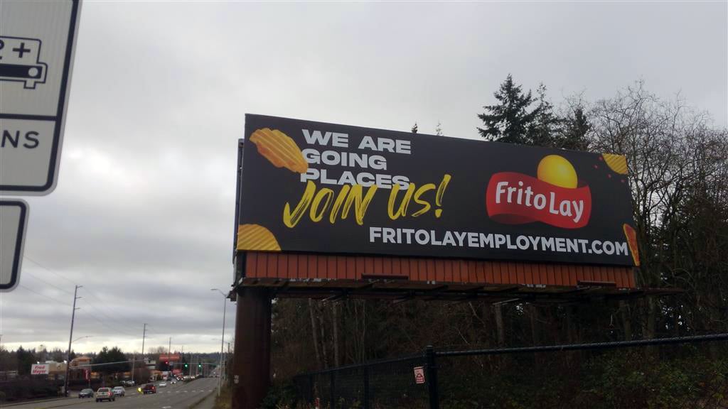 Effective ad by Frito Lay. A billboard with a black background and various chips with the text "we are going places. join us!" next to the frito lay logo and website below