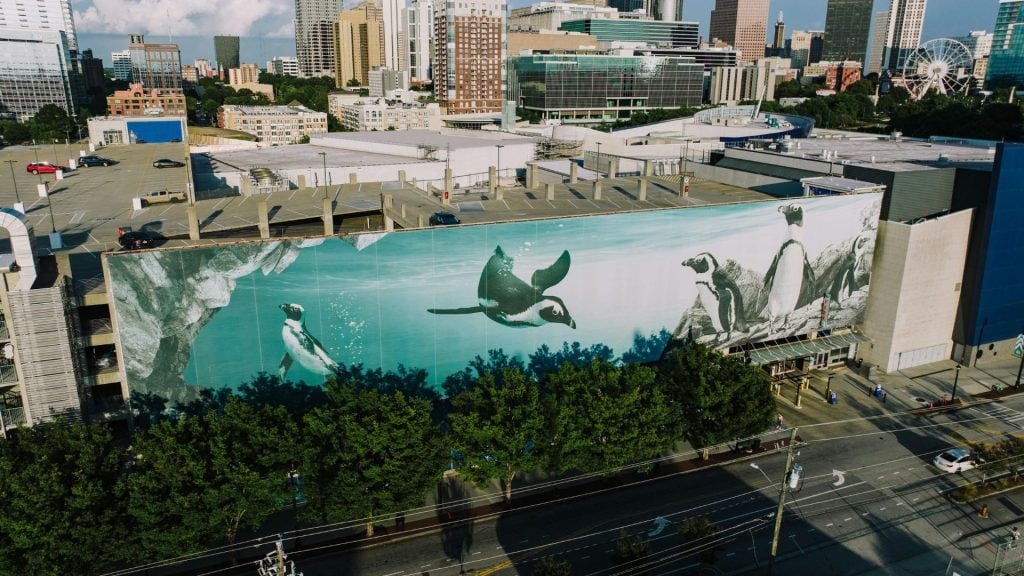 A mural of penguins swimming on the side of a building advertising the aquarium in the city.