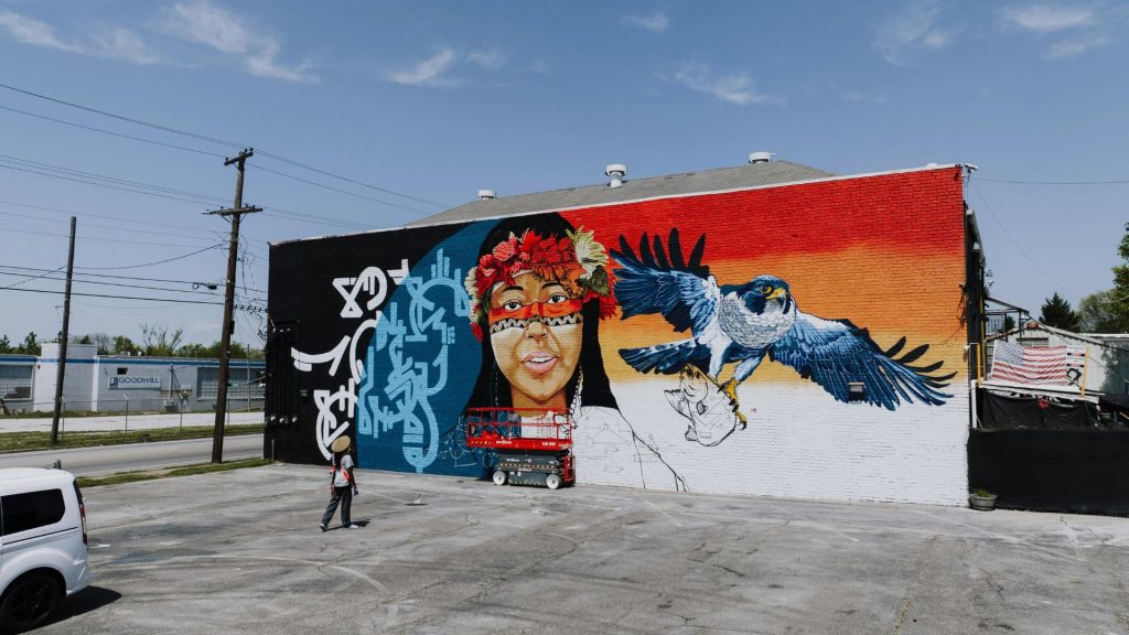 An outdoor wall mural being painted on the back of a building