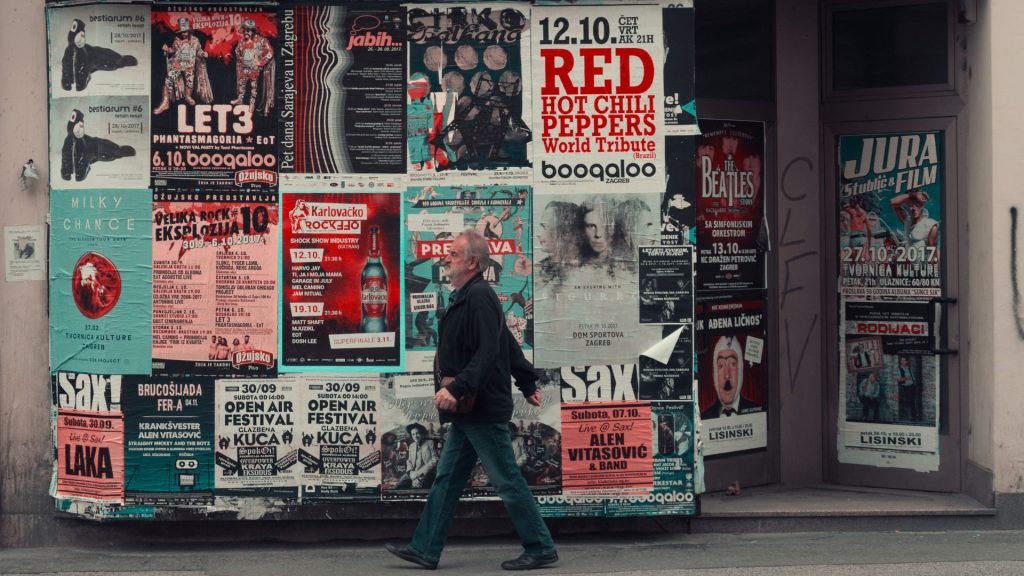 A man walking past a wall of poster advertisements for bands coming into town 