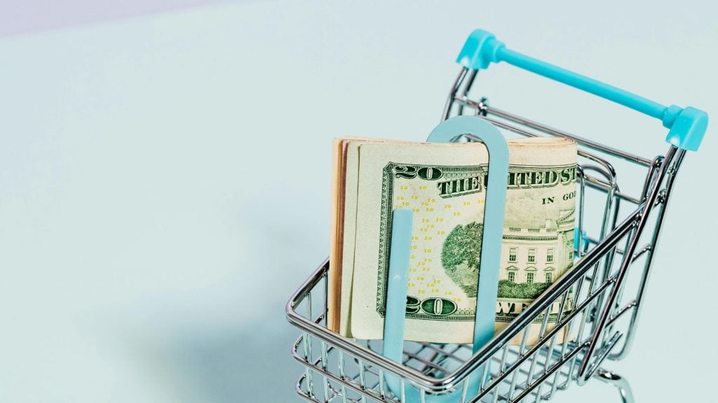 A photo of a miniature shopping cart with a money clip in it with money in it.