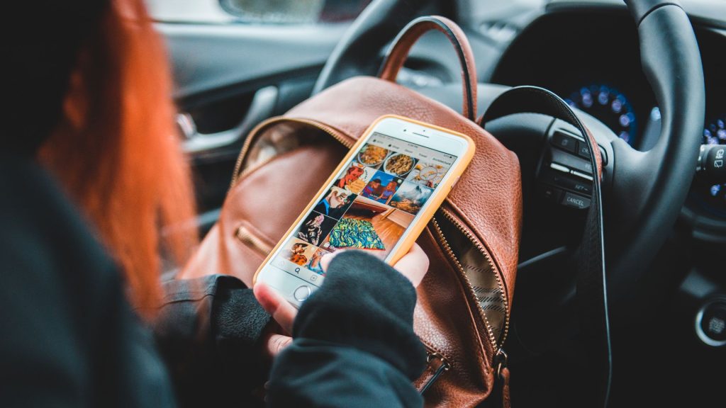 A photo of a women looking at social media ads on her smart phone while sitting in the drivers seat of a car.
