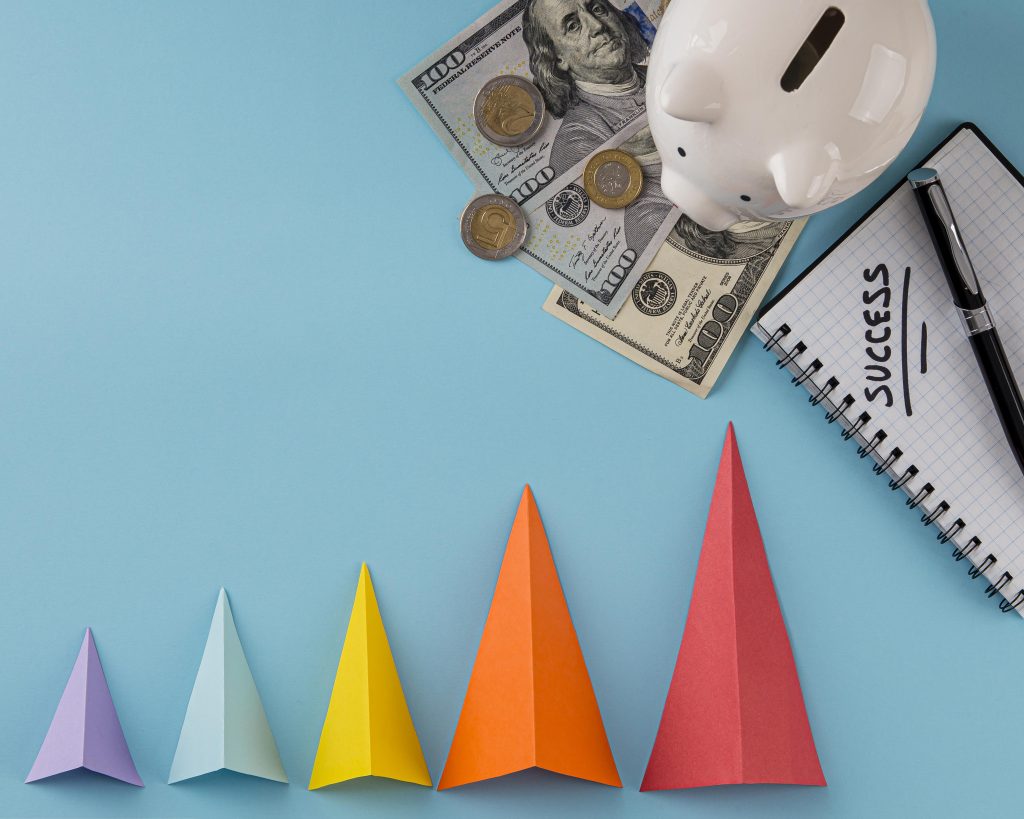 A photo of a piggy bank with money under it and a note book with the word successful next to it with a colorful depiction of effectiveness with a growing pyramid
