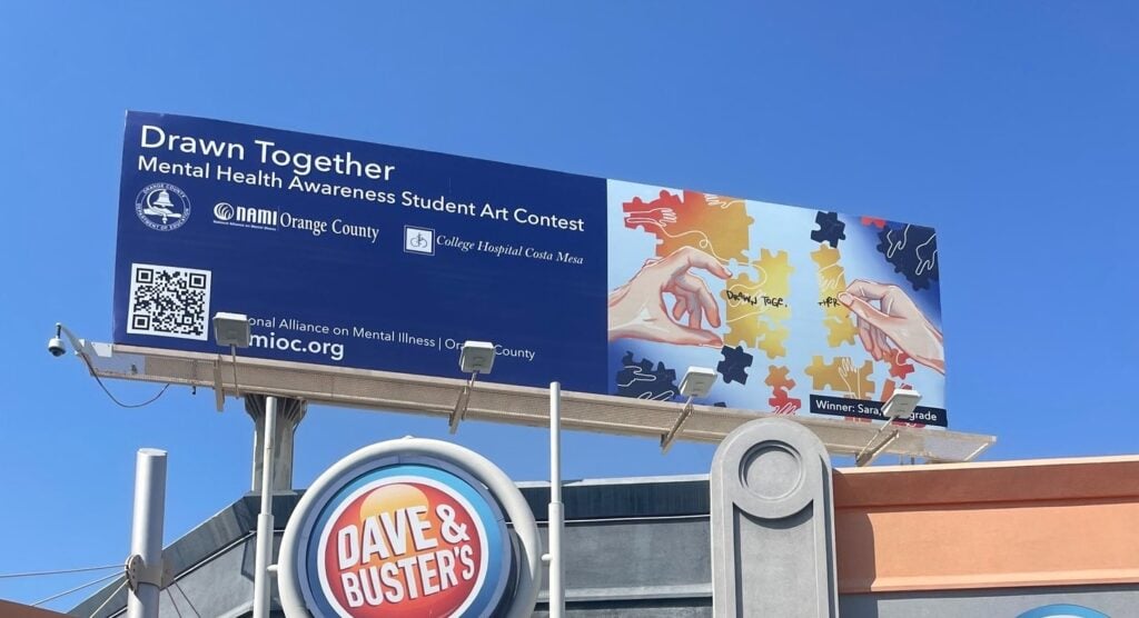 A billboard campaign for mental health awareness student art contest called "Drawn Together" above a Dave&Buster's.