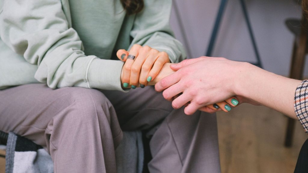 A photo of a person holding another persons hand who is guarded, possibly in a mental health therapist offices