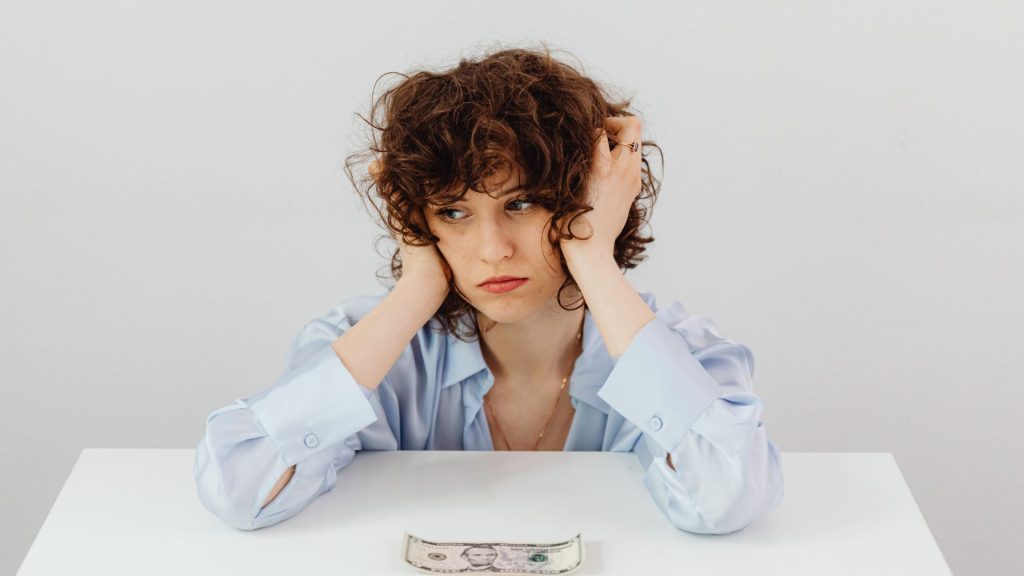 Person sitting at a desk looking stressed while facing a small amount of cash, illustrating budget pressure and common planning challenges often discussed when evaluating the 70/20/10 marketing budget rule and marketing spend decisions.