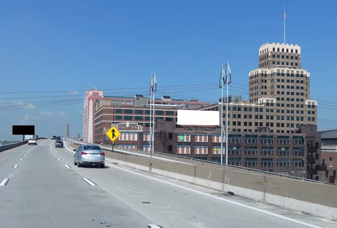 Highway view of a billboard by Gateway Arch area in St. Louis positioned along an elevated roadway, with downtown buildings, traffic, and urban skyline visible in the background.