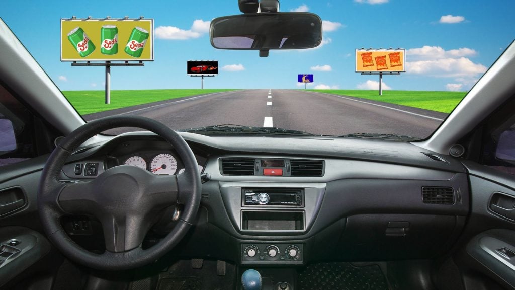 Large digital out-of-home billboard overlooking a busy city roadway at night, illustrating how self driving cars and outdoor media work together to capture passenger attention and create new advertising opportunities along high-traffic urban corridors.