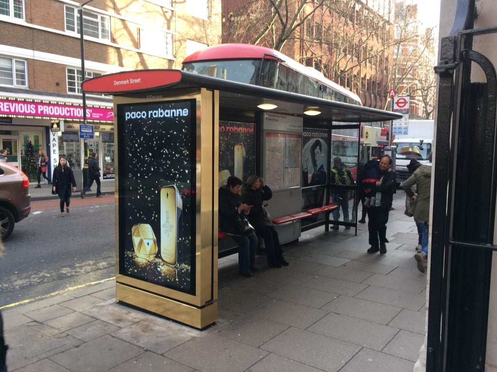 City bus shelter with illuminated display advertising a luxury fragrance brand, showing street-level transit ads as one of the most effective types of outdoor advertising for reaching pedestrians and commuters in high-traffic urban areas.