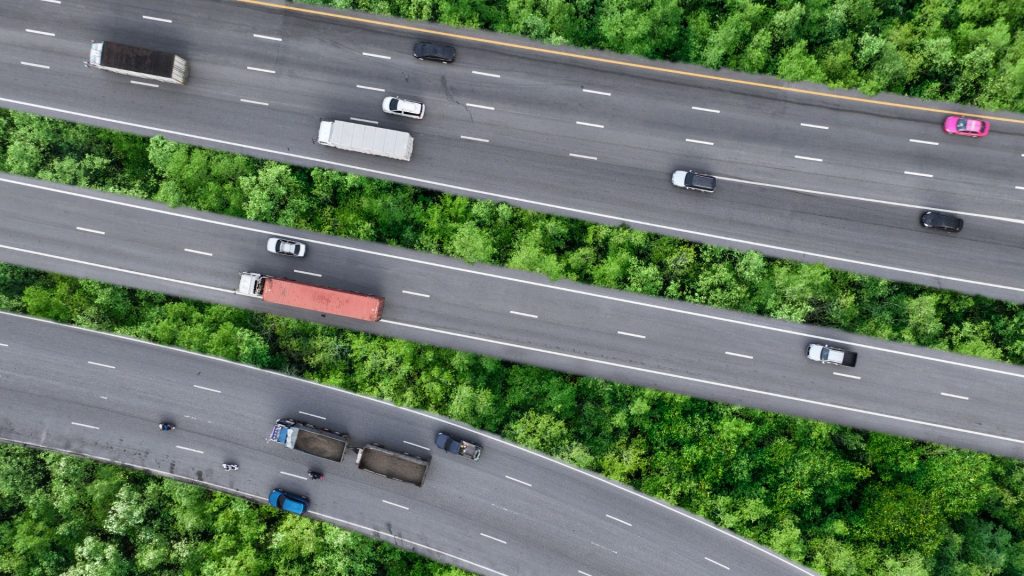 Aerial view of multiple semi-trucks and delivery vehicles traveling on a multi-lane highway, demonstrating the high-reach potential for truck advertising and mobile billboards.