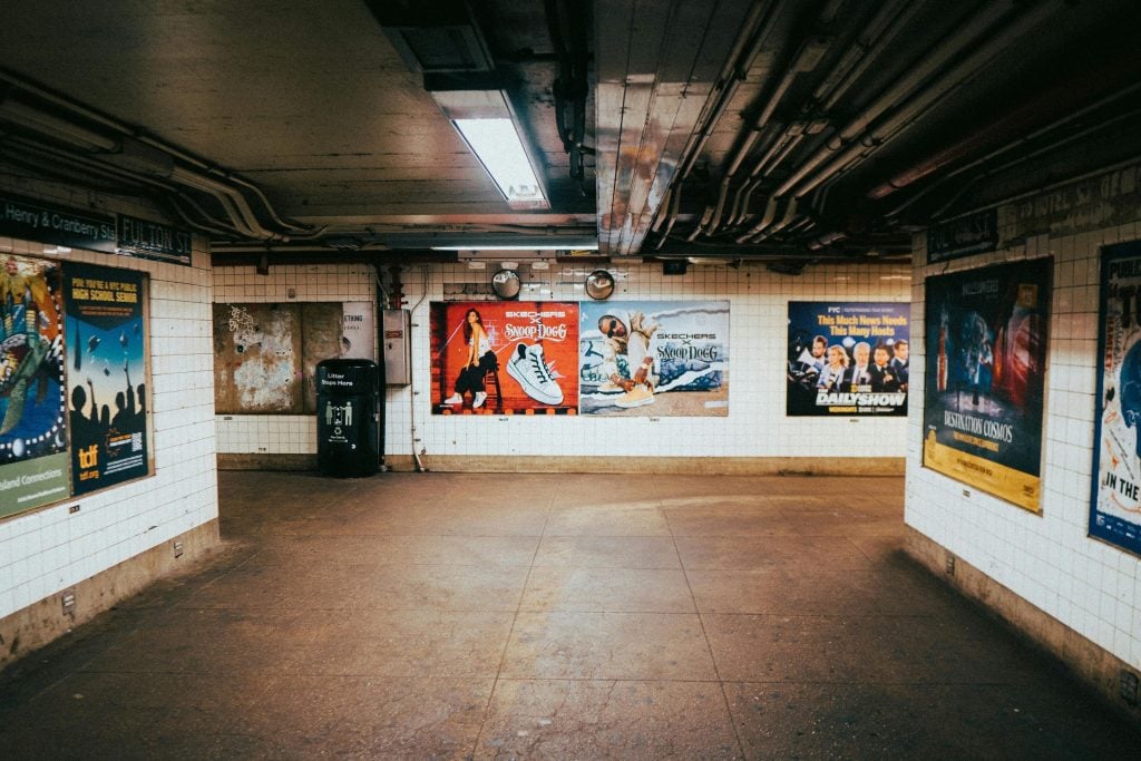 Underground subway station corridor lined with large wall posters and brand advertisements, showcasing transit posters as one of the most common types of outdoor advertising used to reach daily commuters in public transportation spaces.