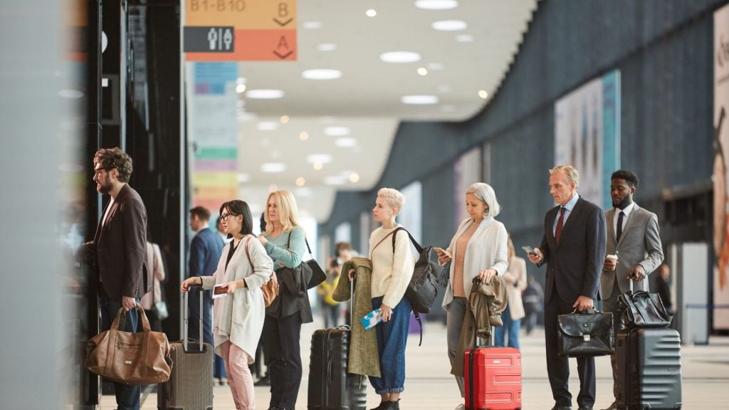 A picture depicting best airport advertising tips with a line of people at an airport looking at their phones with billboards and other ads in the background.