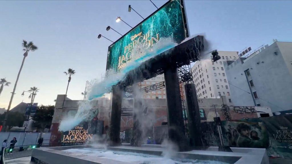 A picture of a tv show/movie billboard promoting the new season of percy jackson that features a waterfall.