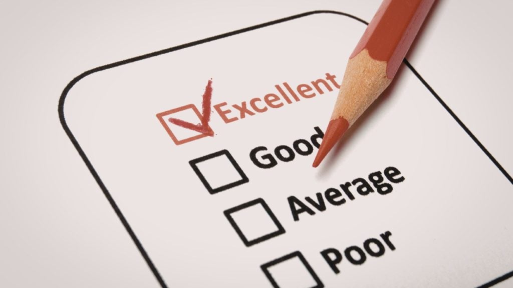 A macro shot of a survey or assessment form with a red pencil checkmark in the "Excellent" box, symbolizing a successful campaign result when learning how to evaluate reach and frequency for outdoor media buys.