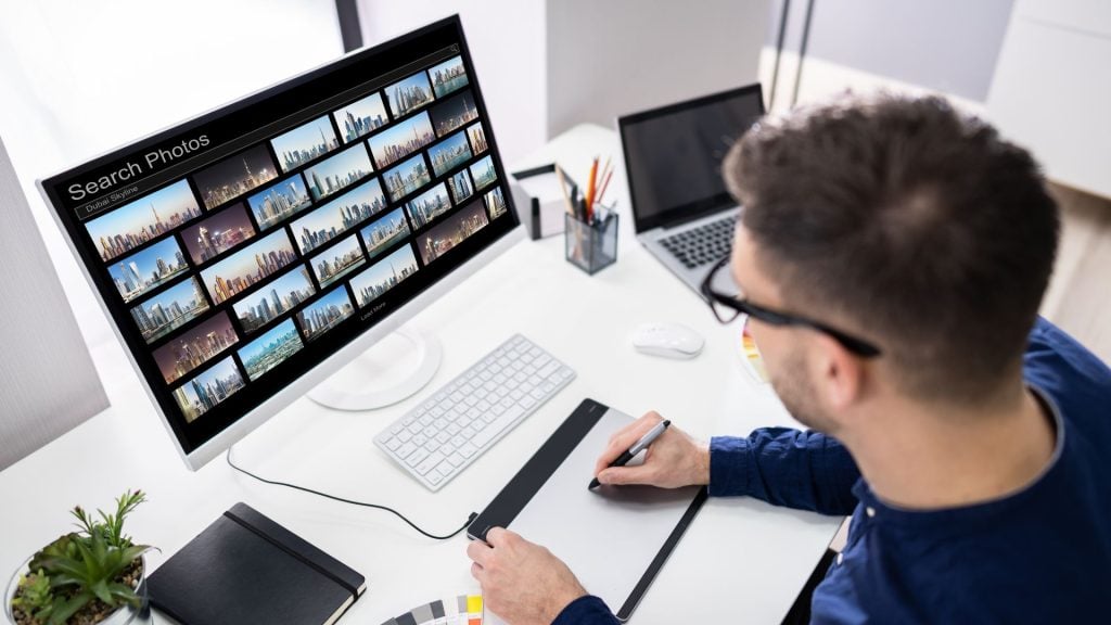 A graphic designer searching for high-quality urban skyline visuals on a monitor, exploring the question, "can i use stock photos for advertising" to enhance professional digital campaigns.