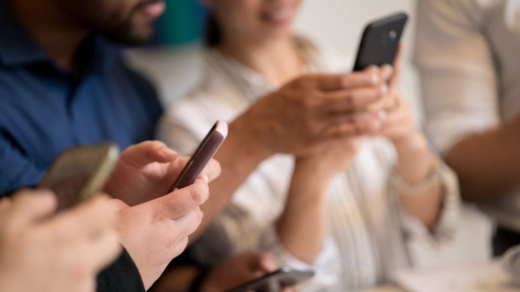 Close-up of multiple people holding smartphones in a group, representing the digital impressions and secondary reach data used in how to evaluate reach and frequency for outdoor media buys.