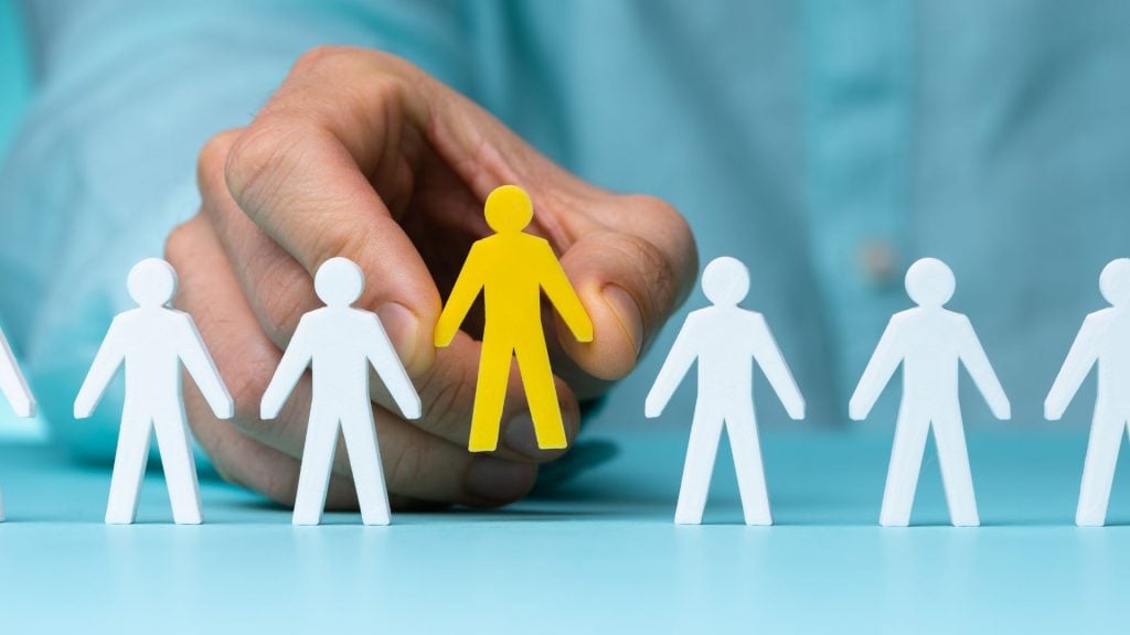 Hand selecting a highlighted customer figure from a group of people, illustrating audience targeting and customer segmentation in a go-to-market strategy.