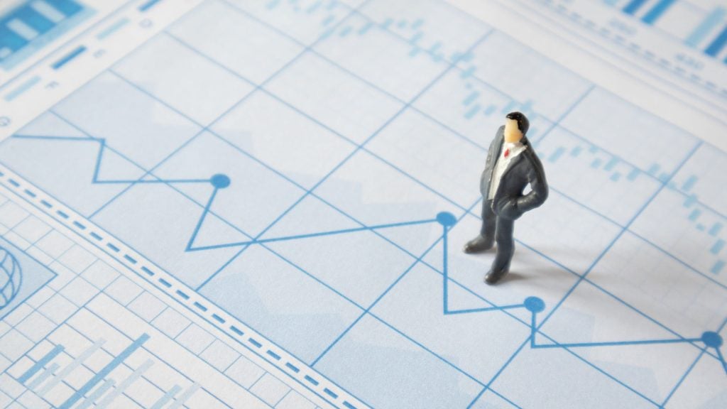 Miniature business person standing on financial charts and graphs, representing data analysis and planning in a what is GTM strategy guide.