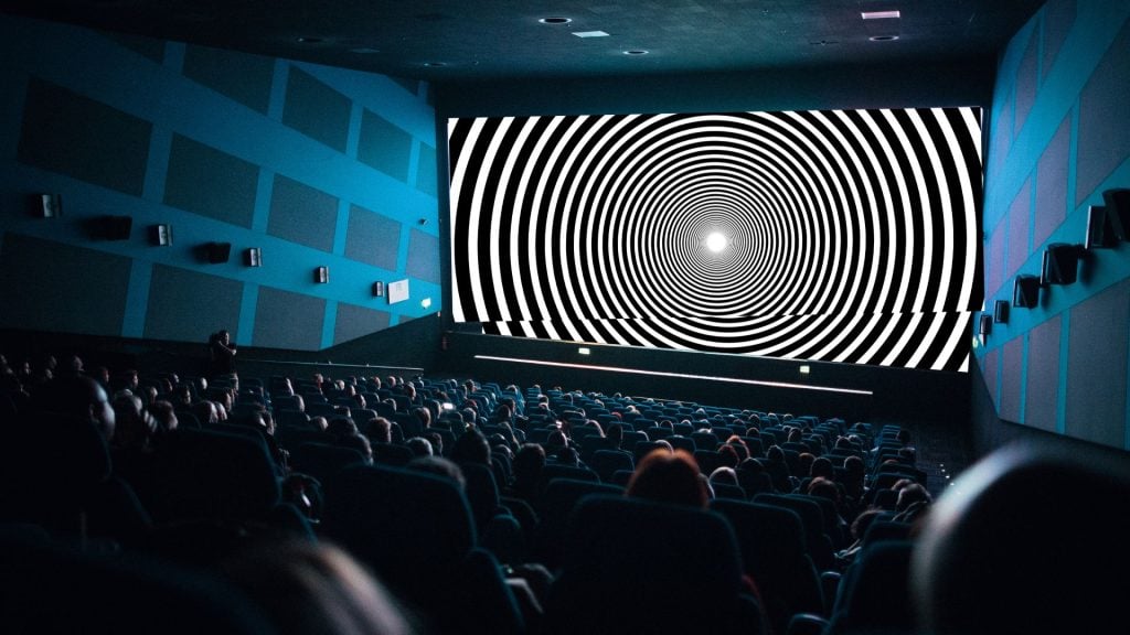 Cinema advertising displayed on a large movie theater screen in front of a captive audience during a theatrical film screening.