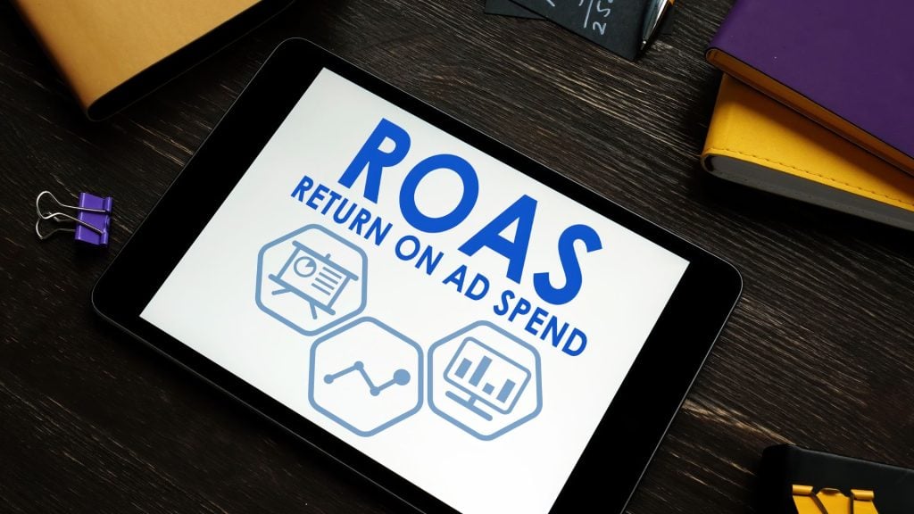 What is ROAS displayed on a tablet with marketing analytics icons representing return on ad spend, campaign performance, and advertising success.