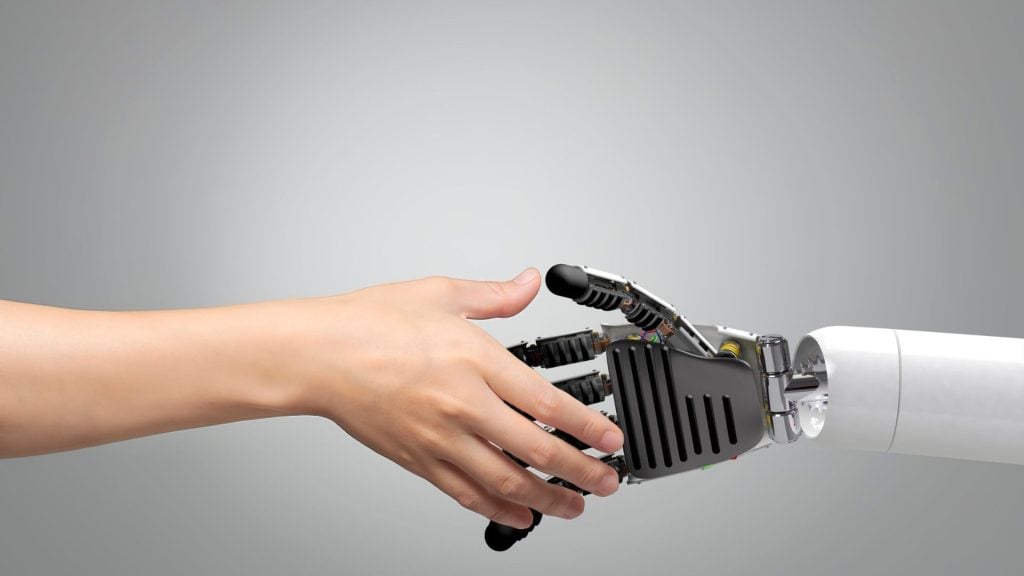 Human and robot shaking hands symbolizes collaboration, emphasizing the role of consumer trust and AI in human-centered technology.