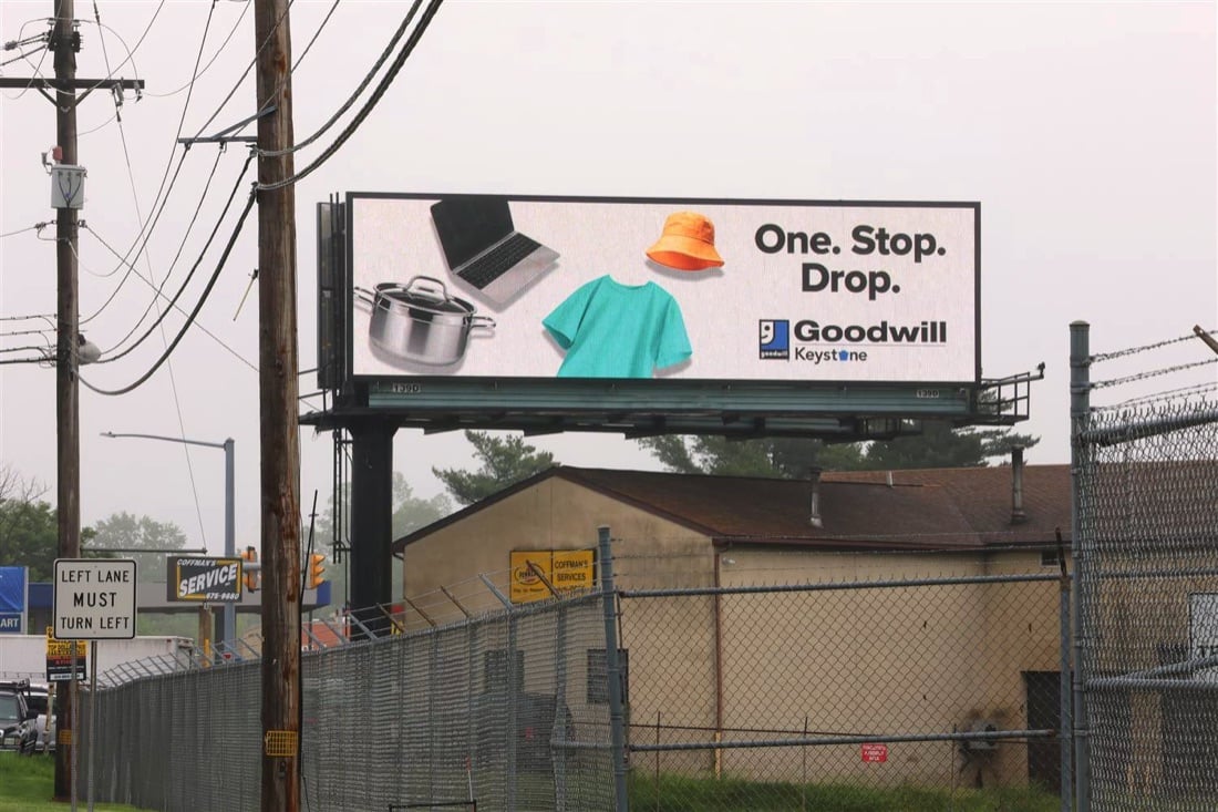 Goodwill digital billboard reading One. Stop. Drop., with a laptop, cooking pot, T-shirt, and bucket hat